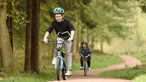 Two children ride bikes through spring trees